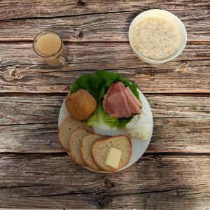 Zdjęcie przedstawia Dietę łatwostrawną: Kawa zbożowa z mlekiem Owsianka budyniowa z bananem i jabłkiem z posypką chia Bułka pszenna długa krojona Masło extra Szynka pieczona na ogniu wieprzowa Sałata zielona Jabłko pieczone z cynamonem Twarożek